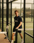 Model wearing Cuera Active WPC Light Weight T-Shirt in Navy, lifestyle action shot on the padel court