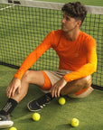 Model wearing Cuera Oncourt LS Layer T-Shirt in Orange, lifestyle action shot on the padel court