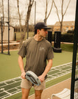 Model wearing Cuera Oncourt Airy Logo T-Shirt in Army, lifestyle action shot on the padel court
