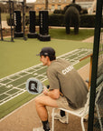 Model wearing Cuera Oncourt Airy Logo T-Shirt in Army, lifestyle action shot on the padel court