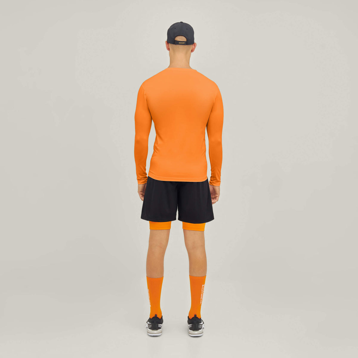 Model wearing Cuera Oncourt LS Layer T-Shirt in Orange, back studio view